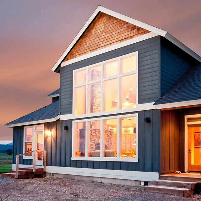 Blue house with large illuminated windows at dusk