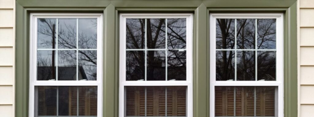 Three new replacement windows with green trim on front of house. Horizontal.