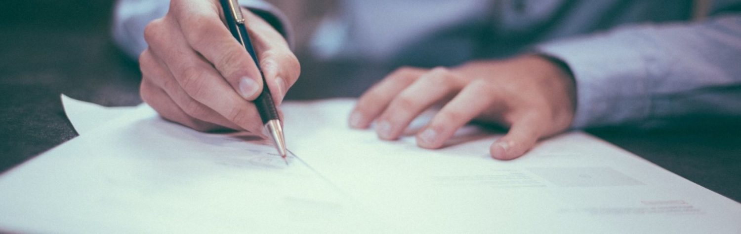 Sales professional writes on a contract with a pen on a desk 