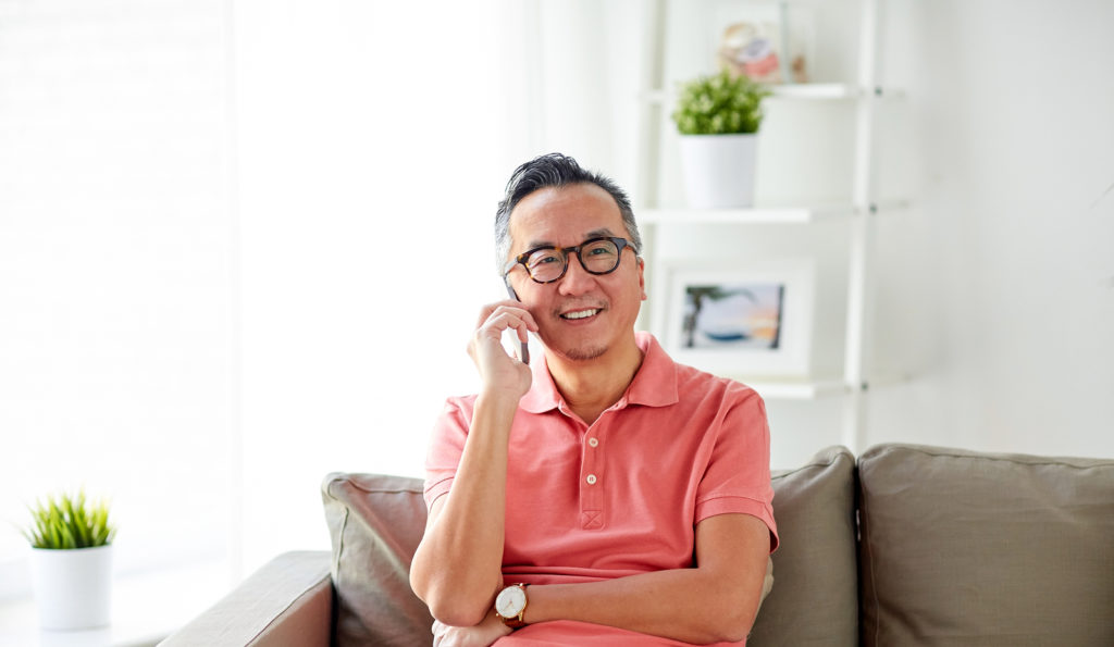 technology, people, lifestyle and communication concept - happy man sitting on sofa calling on smartphone at home