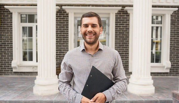Ready to sale. Pleasant cheerful handsome realtor holding folder and expressing positivity while standing outside