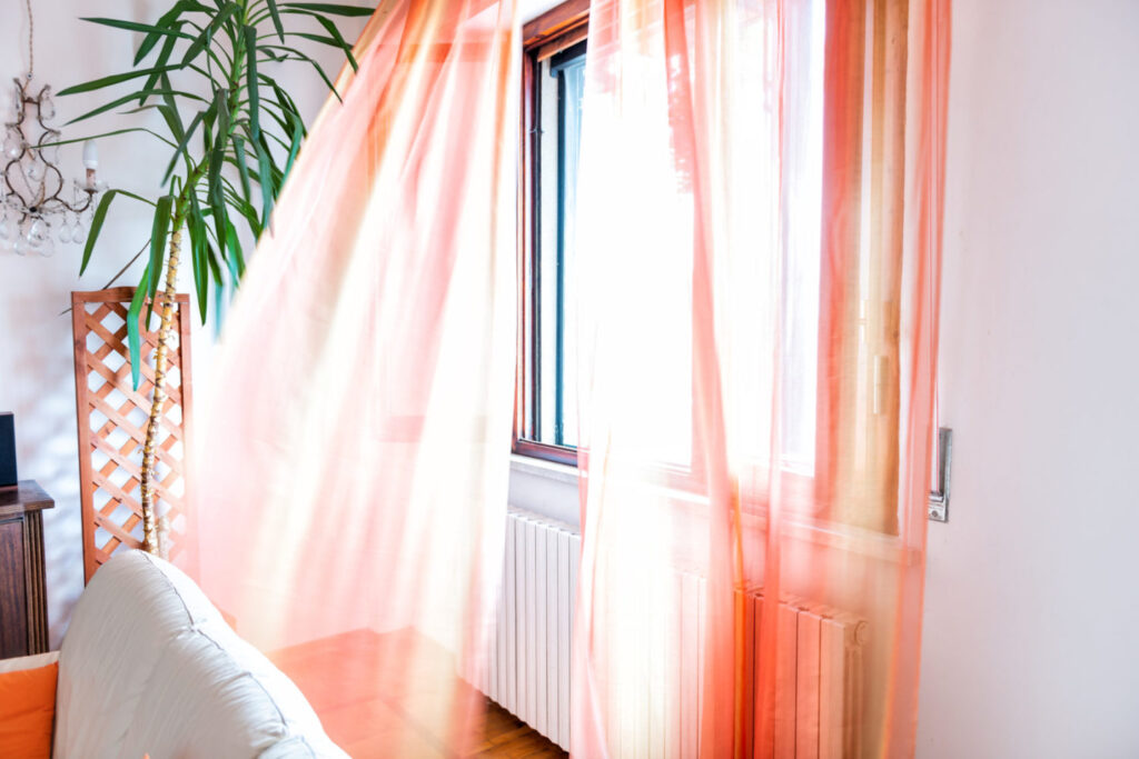 Colorful orange open window curtains blinds in room interior indoors apartment flowing in wind in Italy Open window lets the fresh air circulate in the house
