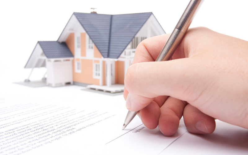 Hand signs a contract in front of a small 3d model of a home