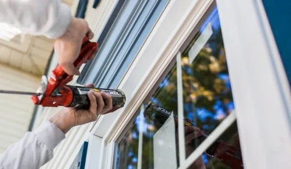 Window Nation installer with foam around a double hung white vinyl window