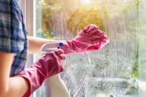 woman in pink glove cleans the inside of window with a rag and spray bottle