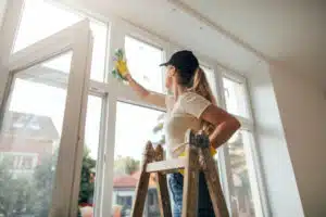 woman cleaning part of a window while standing on a ladder