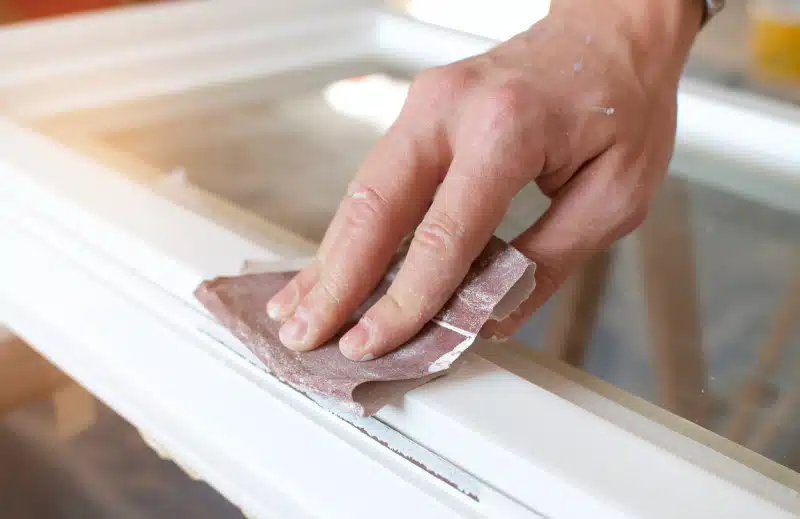 Man using sandpaper on wood window frame