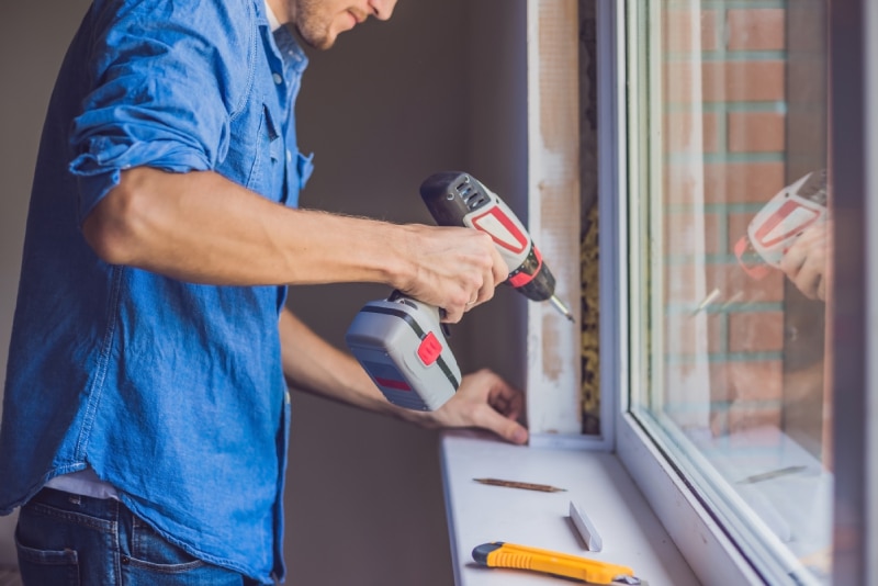 man screwing in a window in his house