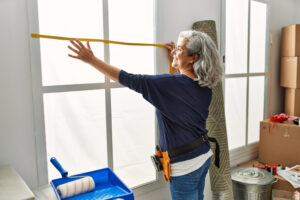 Middle aged grey-haired woman smiles while measuring her window at home